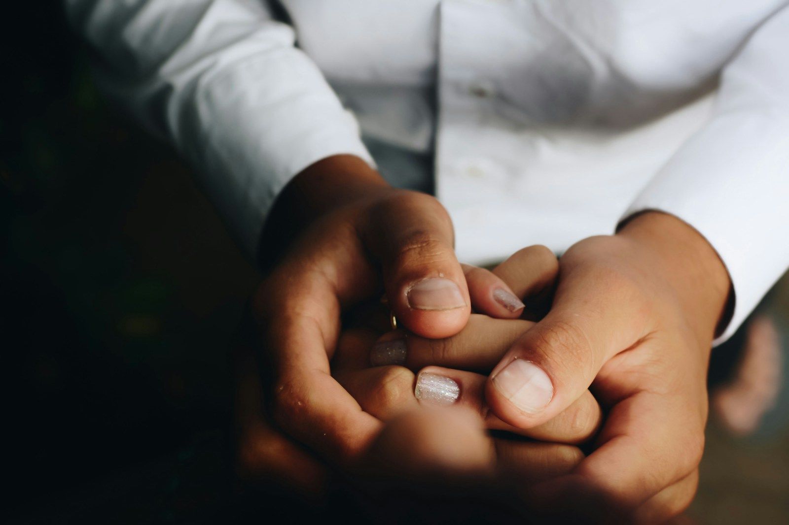 One person's hands holding another's, gently, in warm light
